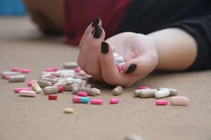 Pastillas en la mano de una persona que esta tirada en el suelo