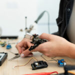 Persona sujetando un cautin sobre una mesa de trabajo