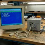 Computadora conectada a un plc, mostrando código en la pantalla y un cable de imagen al frente desconectado.