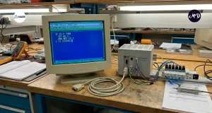 Computadora conectada a un plc, mostrando código en la pantalla y un cable de imagen al frente desconectado.